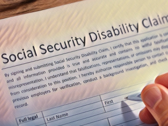 Close-up Of A Person's Hand Filling Social Security Disability Claim Form