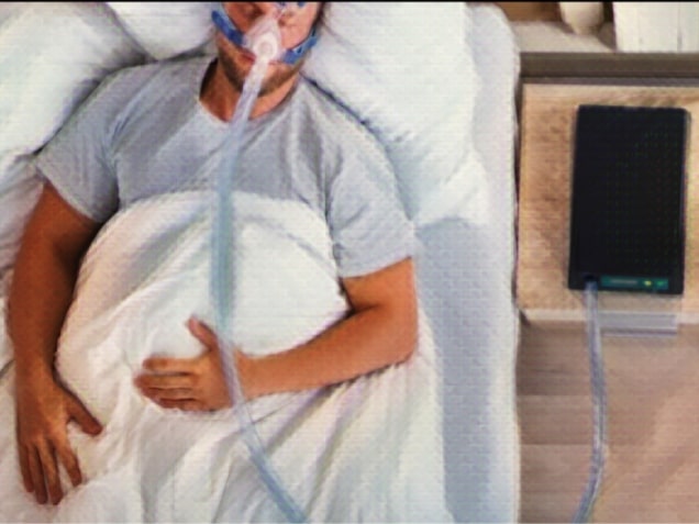 Young man with sleep apnea lying on bed with cpap machine on