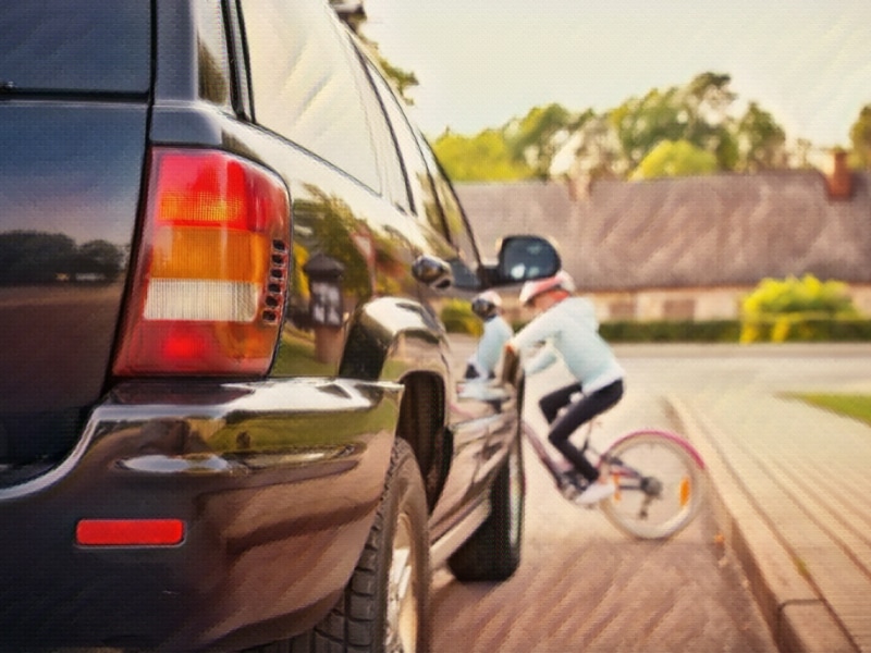 Small girl on the bicycle crosses the road in front of a car. Concept of Why Are Children at Risk for Pedestrian Accident Injuries and Deaths