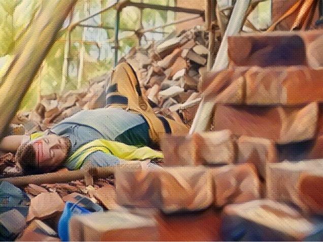 a builder or roofer has fallen from the top elevation of scaffold on a construction site and landed on rubble at the base of the building . He is grimacing in pain .