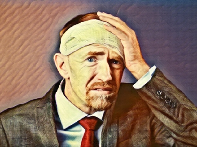 A mature businessman with his head wrapped in bandages, holds his hand to his head, distressed.