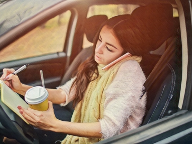 Worker is drinking hot coffee, writing in a notebook and talking on the phone at the same time.