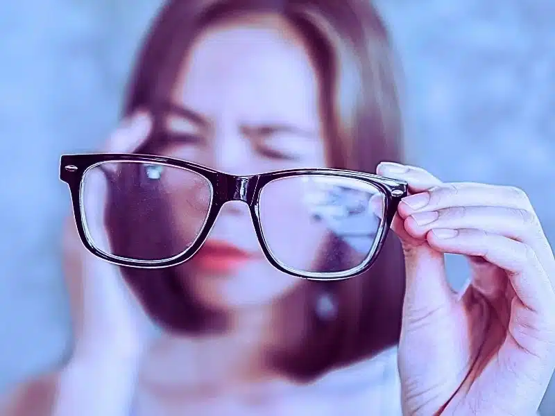 Asian woman holding eyeglasses having headache with eye blur vision. Lawsuit for Elmiron eye damage.